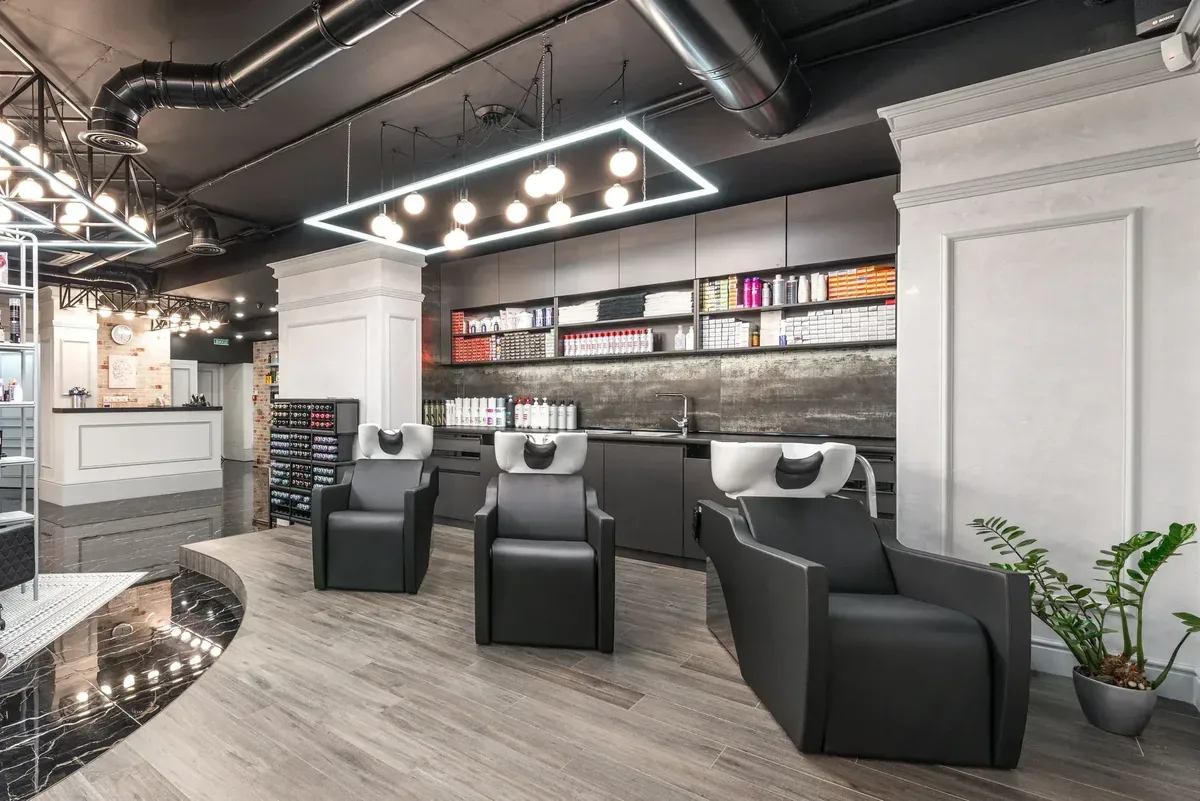 A hair salon with three basin chairs, shelves of hair colour and a reception desk in the background; example image.